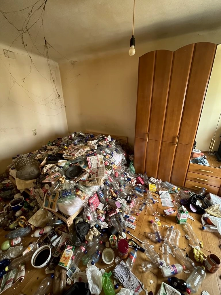 Wohnung vor der Räumung: dichter Müll, leere Flaschen und Verpackungen auf dem Boden vor einem Kleiderschrank.